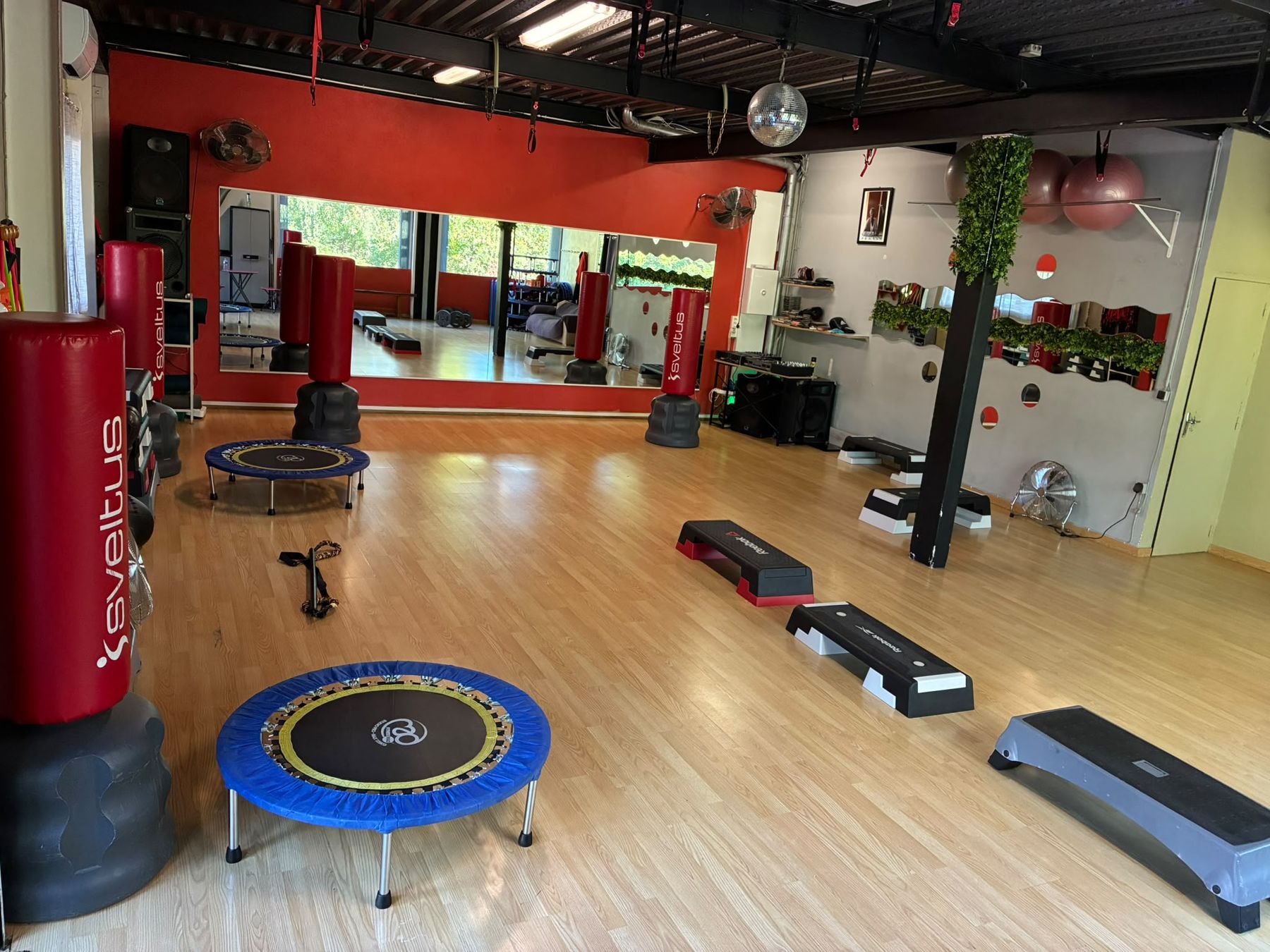 Salle de cours collectifs avec parquet, sacs de frappe, steps et trampolines